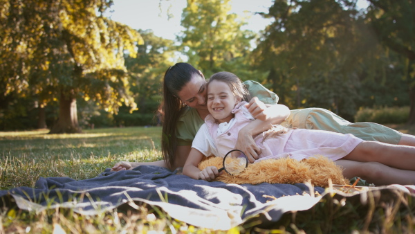 A small girl with mother resting in a park, lying on the blanket.