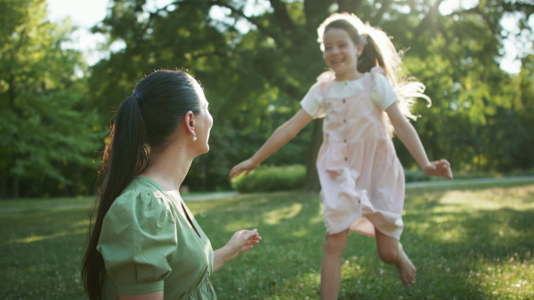 A small girl running to her mother resting in a park on blanket.