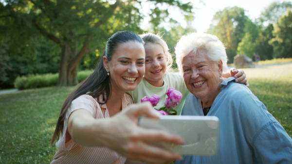 A small girl with mother and grandmother in a park, taking selfie when celebrating birthday.