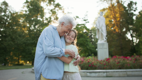 A small girl with grandmother on a walk in park, looking at each other and hugging