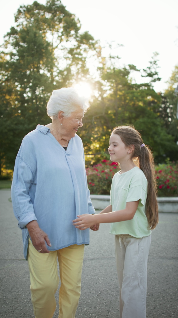 A vertical footage of small girl with grandmother on a walk in park, looking at each other and hugging