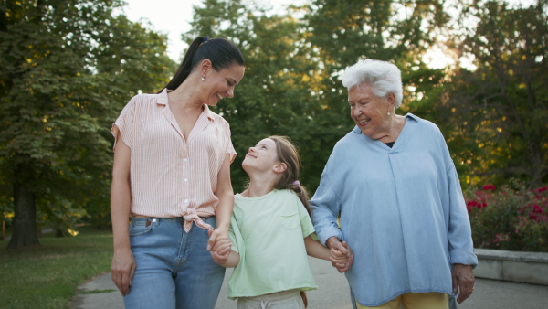 A small girl with mother and grandmother in a park, walking in park.