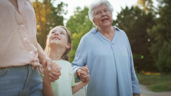 A small girl with mother and grandmother in a park, walking in park.