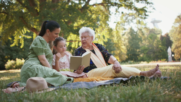 A small girl with mother and grandmother resting in a park, reading a book.