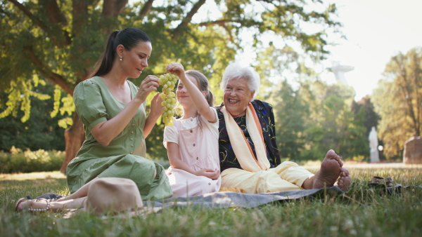 A small girl with mother and grandmother resting in a park, having picnic.