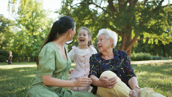 A small girl with mother and grandmother resting in a park, talking.