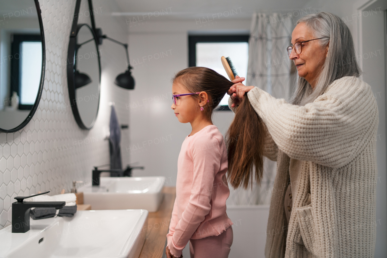 A senior grandmother and granddaughter standing indoors in bathroom, daily routine concept.