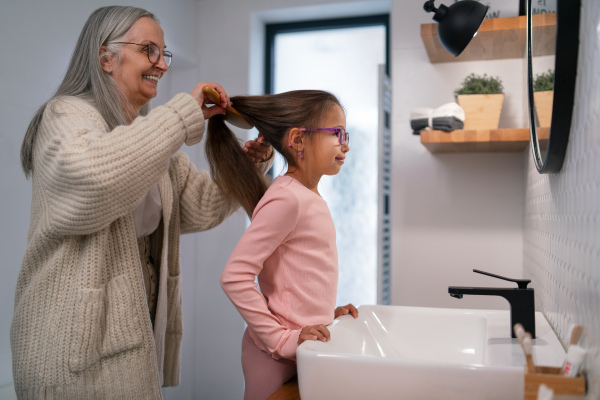 A senior grandmother and granddaughter standing indoors in bathroom, daily routine concept.