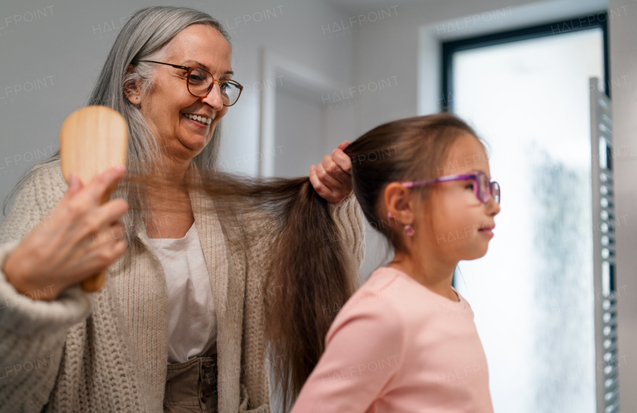 A senior grandmother and granddaughter standing indoors in bathroom, daily routine concept.