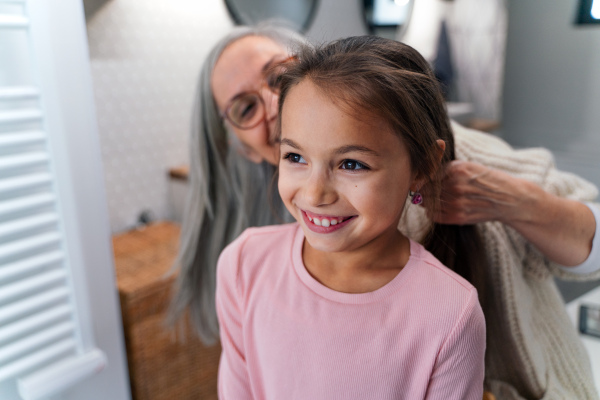 A senior grandmother and granddaughter standing indoors in bathroom, daily routine concept.