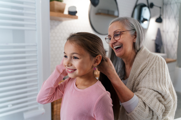 A senior grandmother and granddaughter standing indoors in bathroom, daily routine concept.