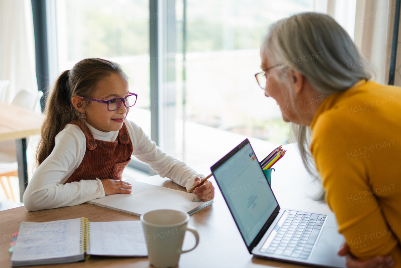 A small girl with senior grandmother doing homework at home.