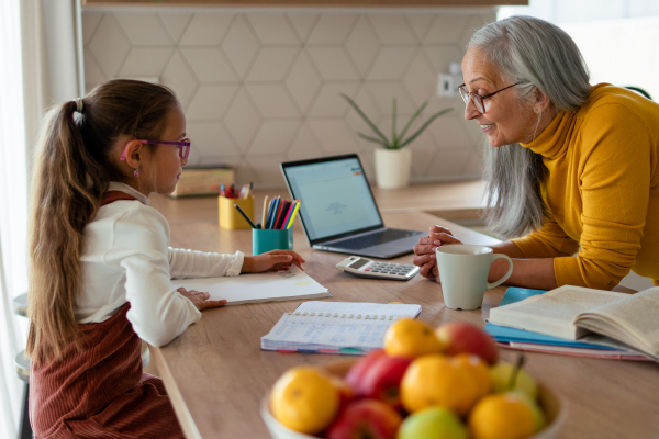 A small girl with senior grandmother doing homework at home.