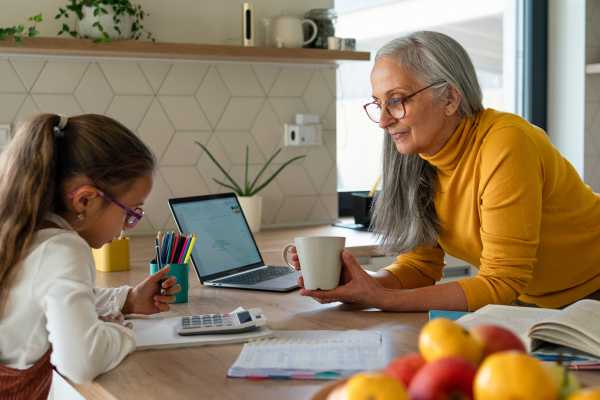 A small girl with senior grandmother doing homework at home.