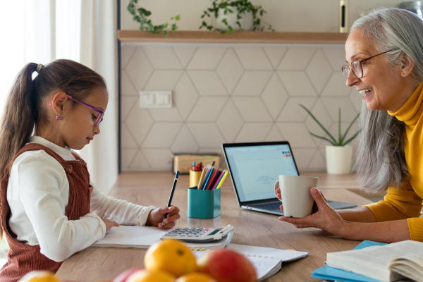 A small girl with senior grandmother doing homework at home.