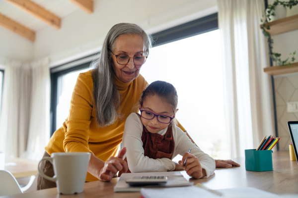 A small girl with senior grandmother doing homework at home.