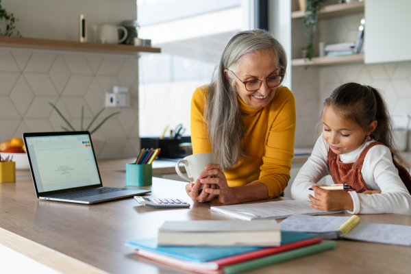 A small girl with senior grandmother doing homework at home.