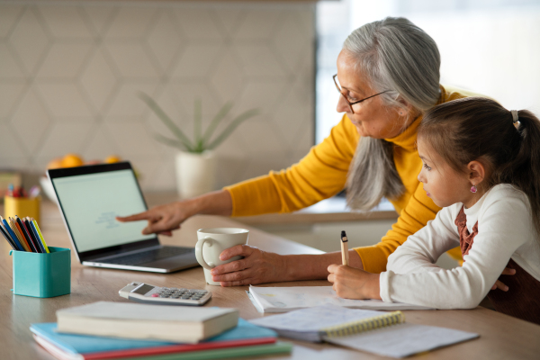 A small girl with senior grandmother doing homework at home.