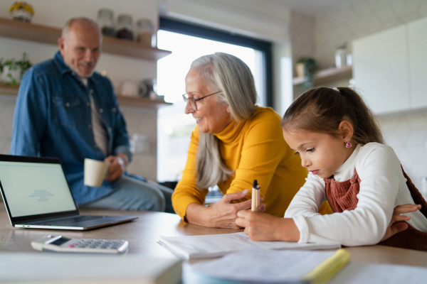 A small girl with senior grandparents doing maths homework at home.