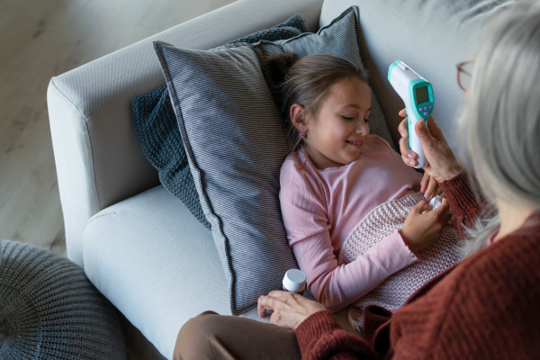 A grandmother taking care of her ill grandchild lying on sofa