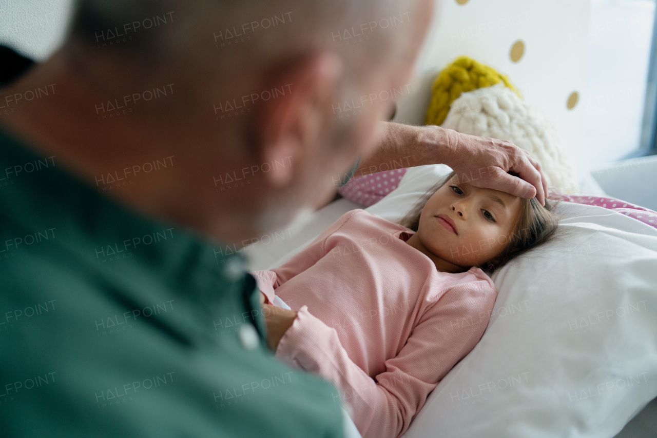 A grandfather taking care of his ill granddaughter lying in bed.