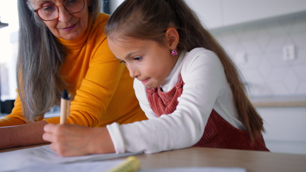 A small girl with grandmother doing homework at home.