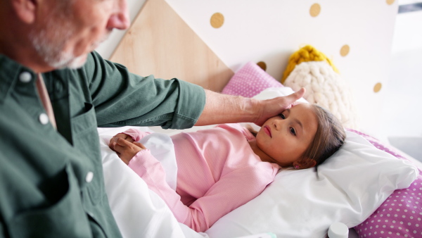 A grandfather taking care of his ill granddaughter lying in bed.