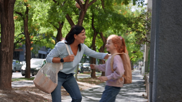 A happy schoolgirl hugging his grandmother waiting for her after school outdoors in street.