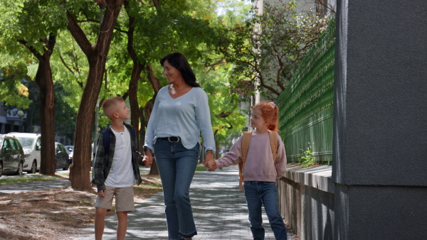 A happy grandmother taking grandchildren home from school, walking outdoors in street.