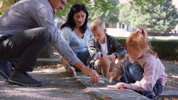 A senior couple with grandchildren drawing with chalks on pavement outdoors in park.