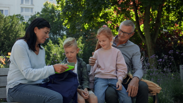 Happy grandparents sitting with grandchildren on a bench in park and having snack