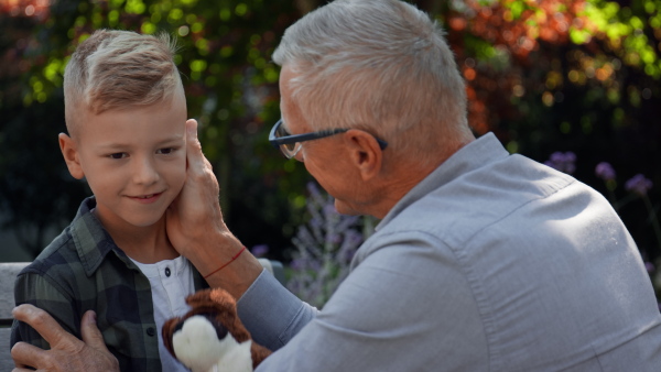 A granfather stroking his little grandson outdoors in park.