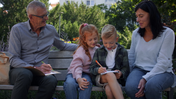 A senior couple with grandchildren sitting on bench and doing homewrok outdoors in park.