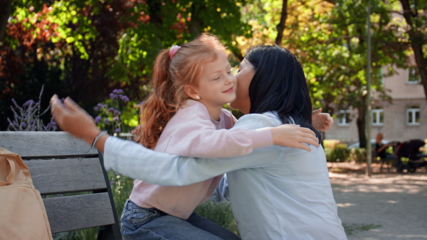 A happy little girl hugging her grandmother outdoors in park.