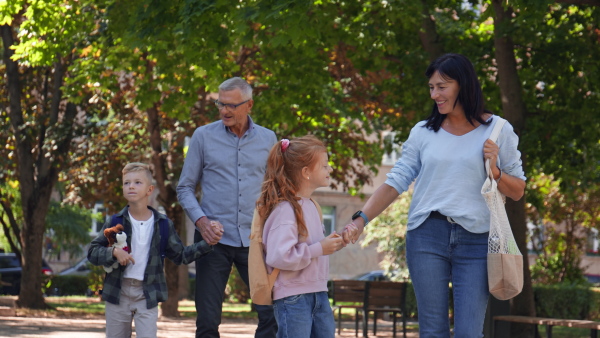 Happy grandparents taking grandchildren home from school, walking outdoors in a street.