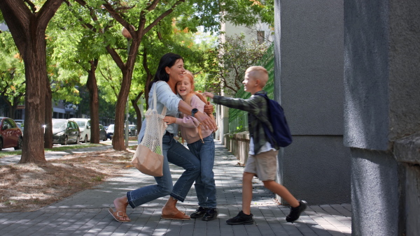 Happy schoolchildren running to their grandmother waiting for them after school outdoors in a street.