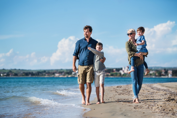 Young family with two small children walking barefoot outdoors on beach.