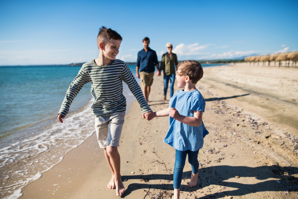 Young family with two small children walking barefoot outdoors on beach, having fun.