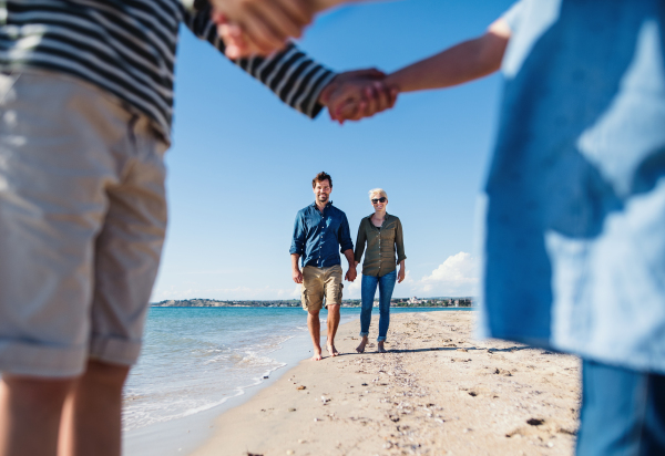 Young family with two small children walking and standing barefoot outdoors on beach.