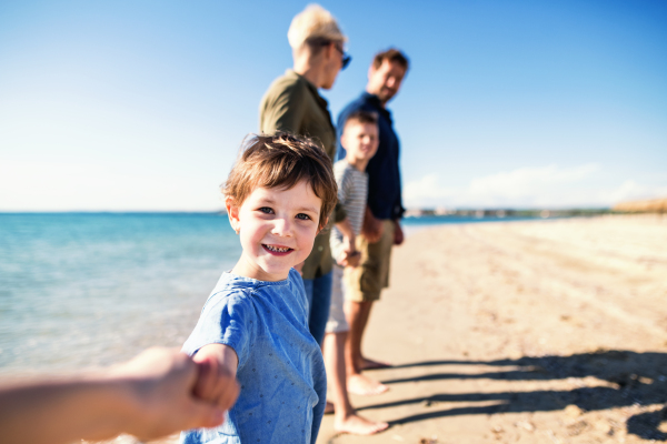 Young family with two small children standing barefoot outdoors on beach, holding hands.