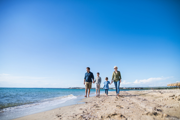 Young family with two small children walking barefoot outdoors on beach.