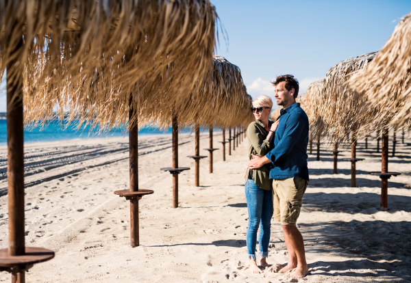 Young couple standing outdoors among straw umbrellas on beach, hugging. Copy space.