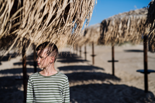 A small boy standing among straw parasols outdoors on beach. Copy space.