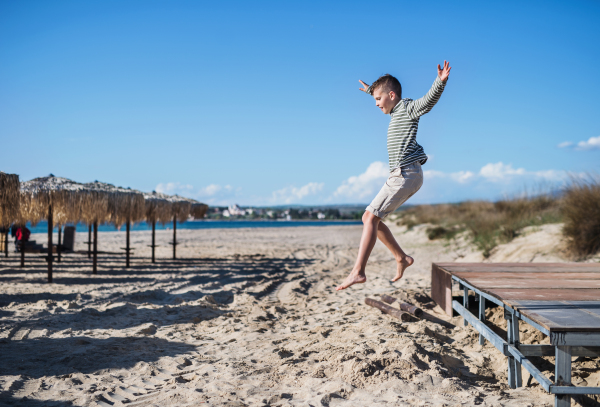 A cheerful small boy playing outdoors on sand beach, jumping.