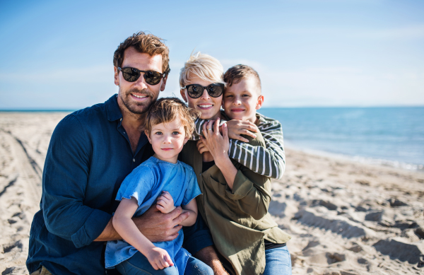 Portrait of young family with two small children sitting outdoors on beach.