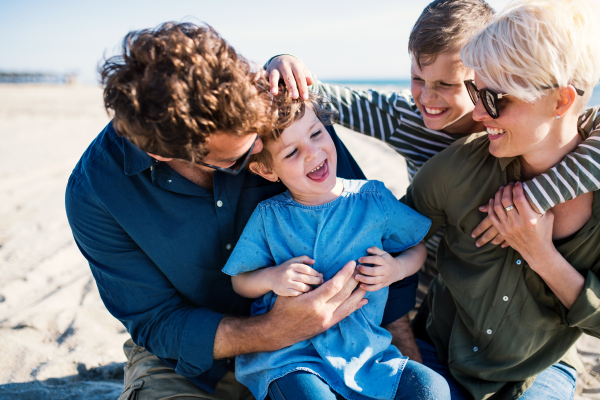 Portrait of young family with two small children sitting outdoors on beach, having fun.