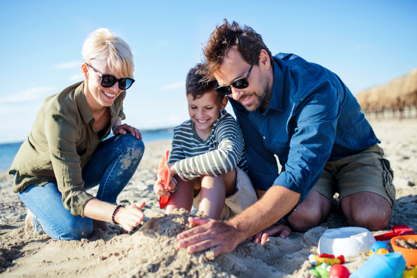 A young family with small boy sitting outdoors on beach, playing.