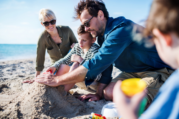 Young family with two small children sitting outdoors on beach, playing with sand.