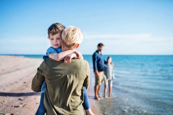 Young family with two small children walking barefoot outdoors on beach.