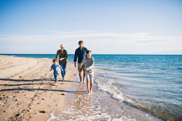 Young family with two small children running barefoot outdoors on beach.